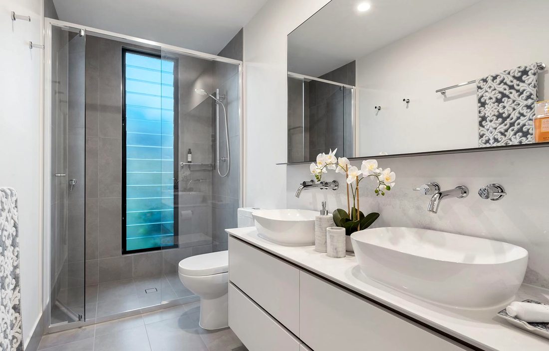 A bathroom with a stone basin, a glass shower and flowers on the counter