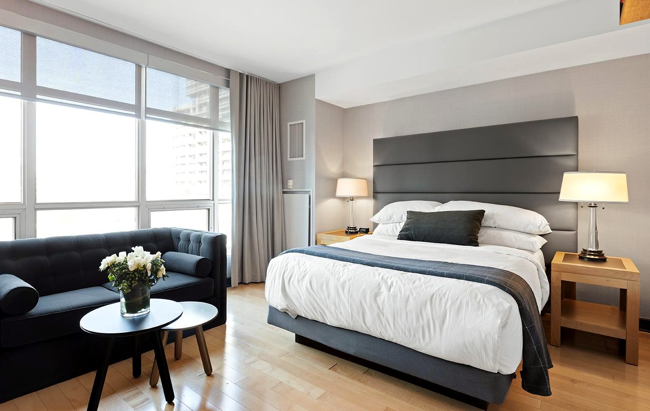 A corner room with a sofa under a tall window and a bed against the inner wall